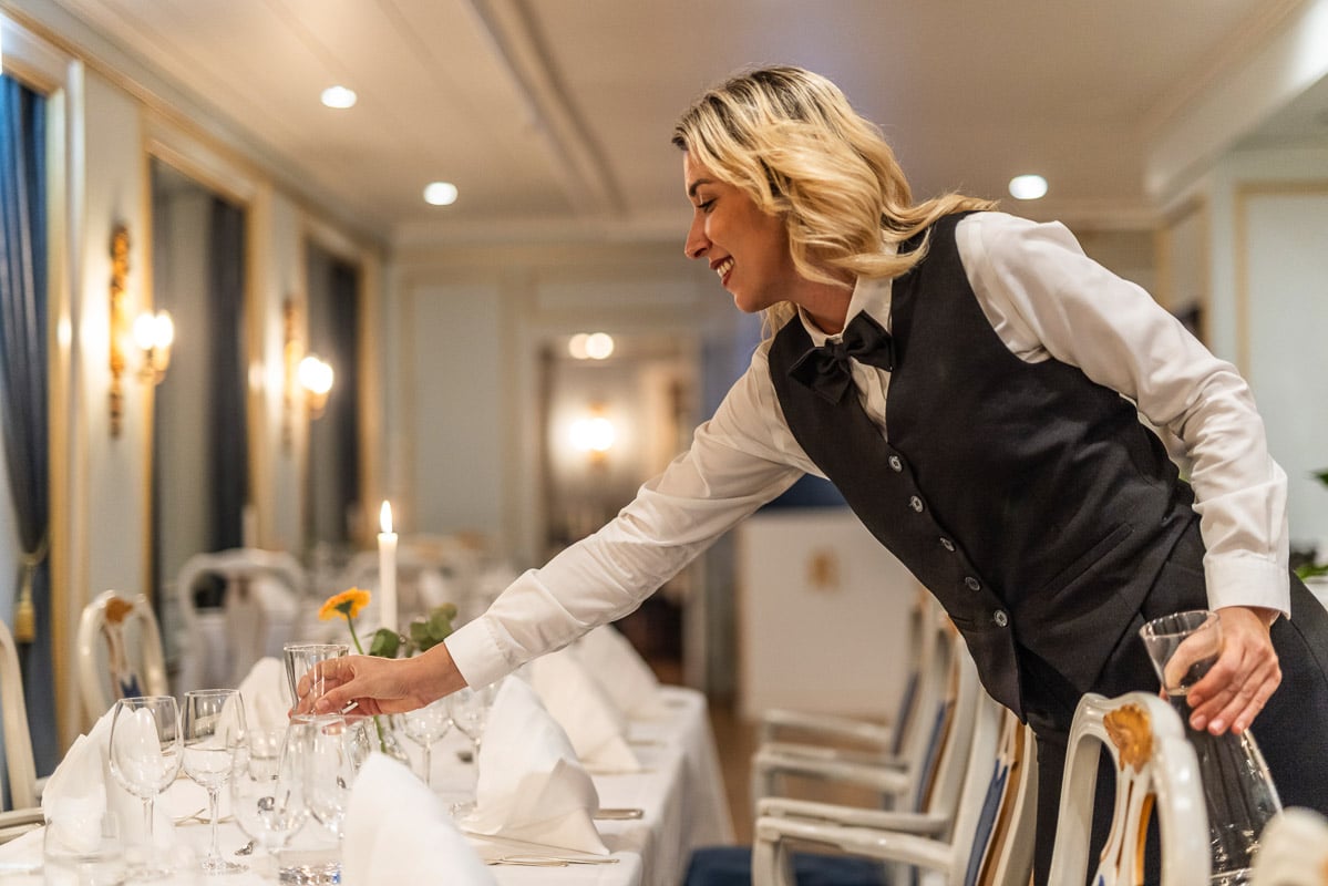 Servitør dekker bord i Restaurant Munch på Refsnes Gods i Moss – herskapelig hotell fra 1767 kjent for personlig vertskap og eleganse.