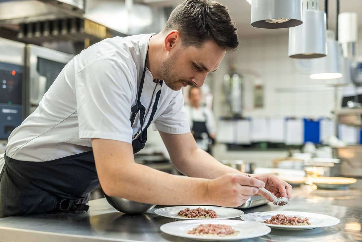 Kokk strør urter over rett på Restaurant Munch, Refsnes Gods i Moss – gourmetrestaurant med fokus på detaljer.